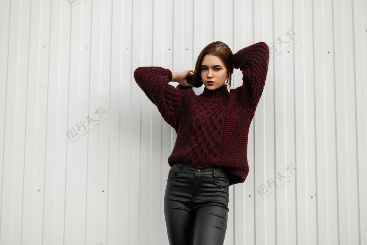 模型穿着紫红色毛衣的时髦年轻女子在一堵白墙附近的城市里摆姿势衣服紧身裤墙