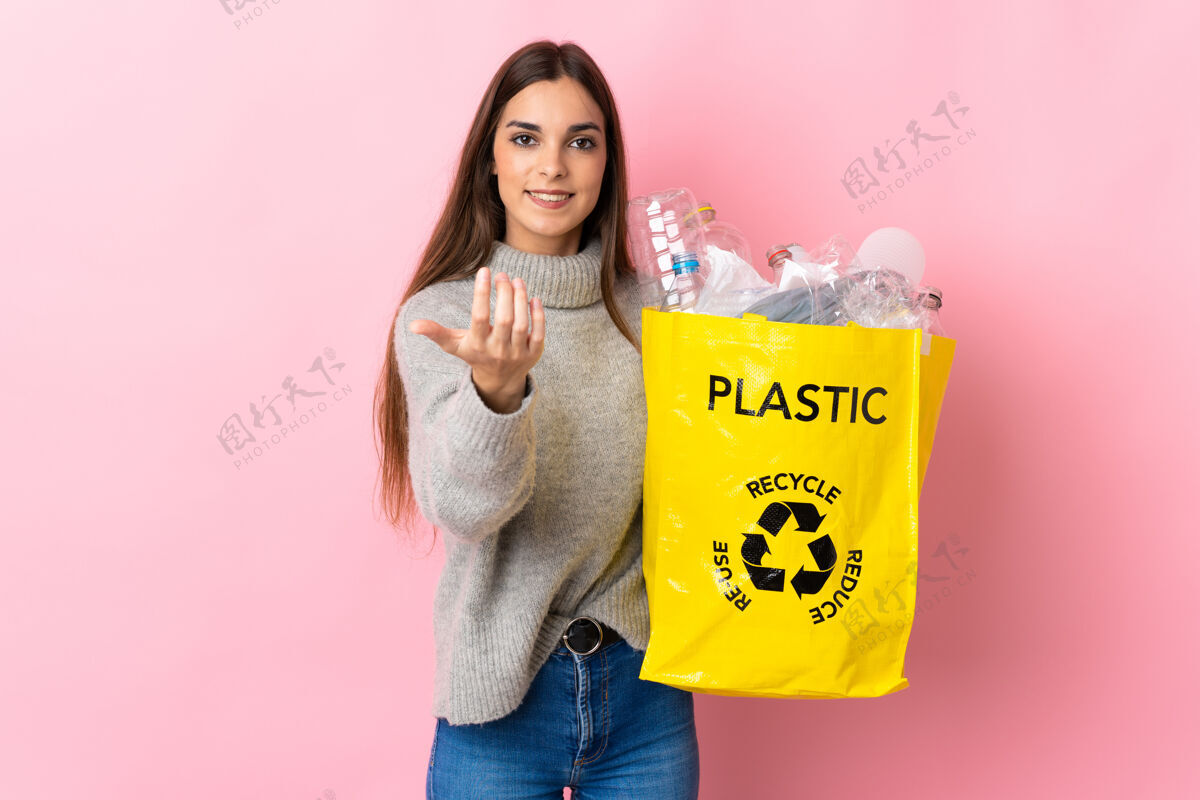 环境一位年轻的白人妇女拿着一个装满塑料瓶的袋子 在粉红色的背景下 邀请大家一起去回收手高兴你来了女人回收废物
