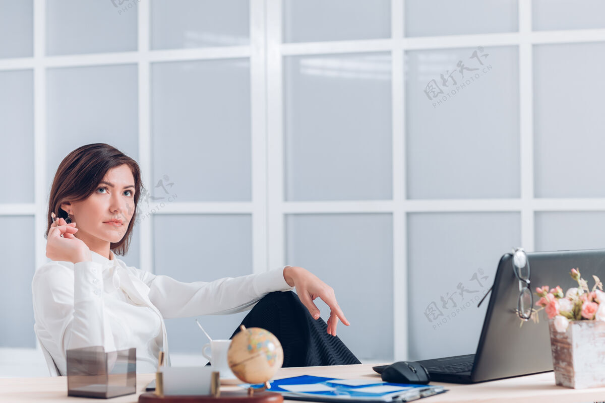坐着漂亮的女商人在办公室的办公桌旁抽烟和工作桌子美女窗口