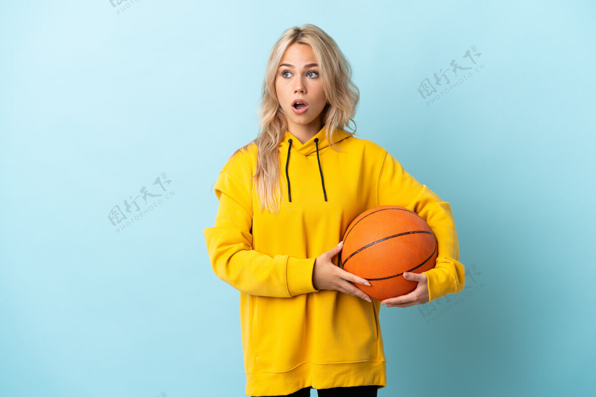 稍后年轻的俄罗斯女子打篮球孤立在蓝色做惊喜的手势 同时向一边看担心手势震惊