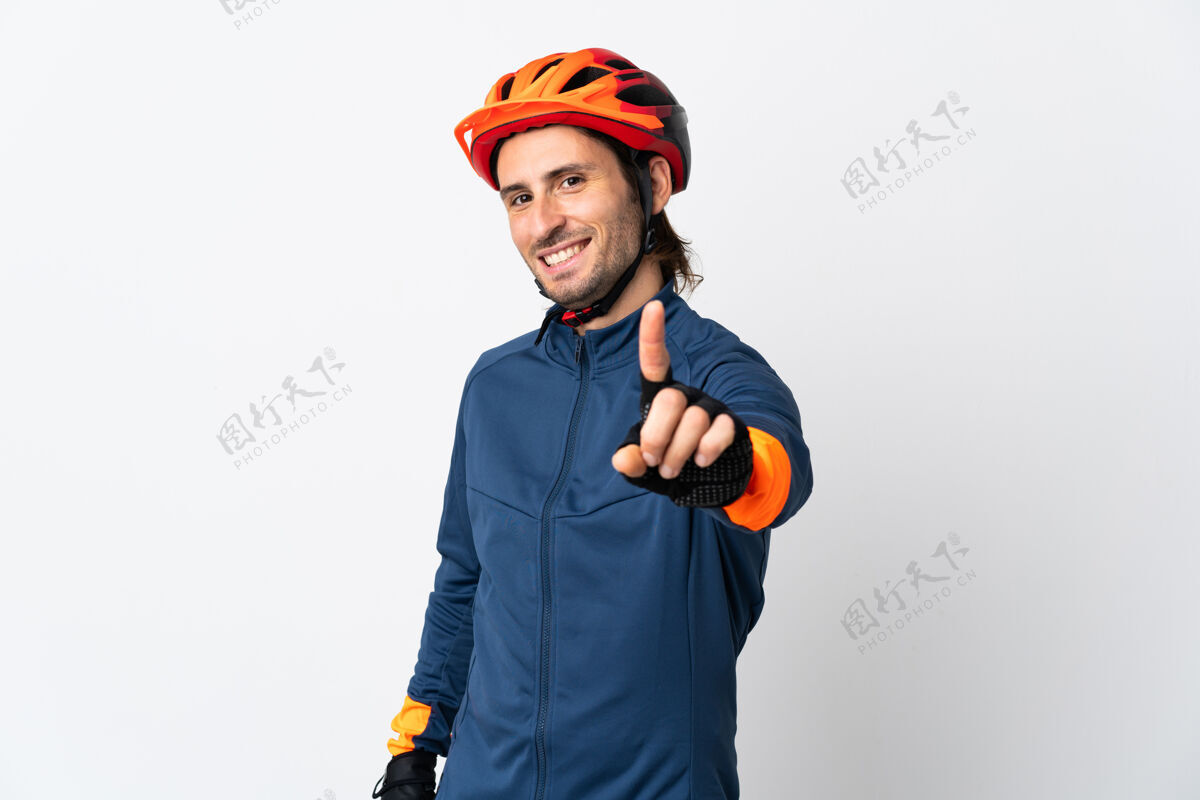 人一个骑自行车的年轻人被隔离在白墙上 伸出一根手指第一点手指