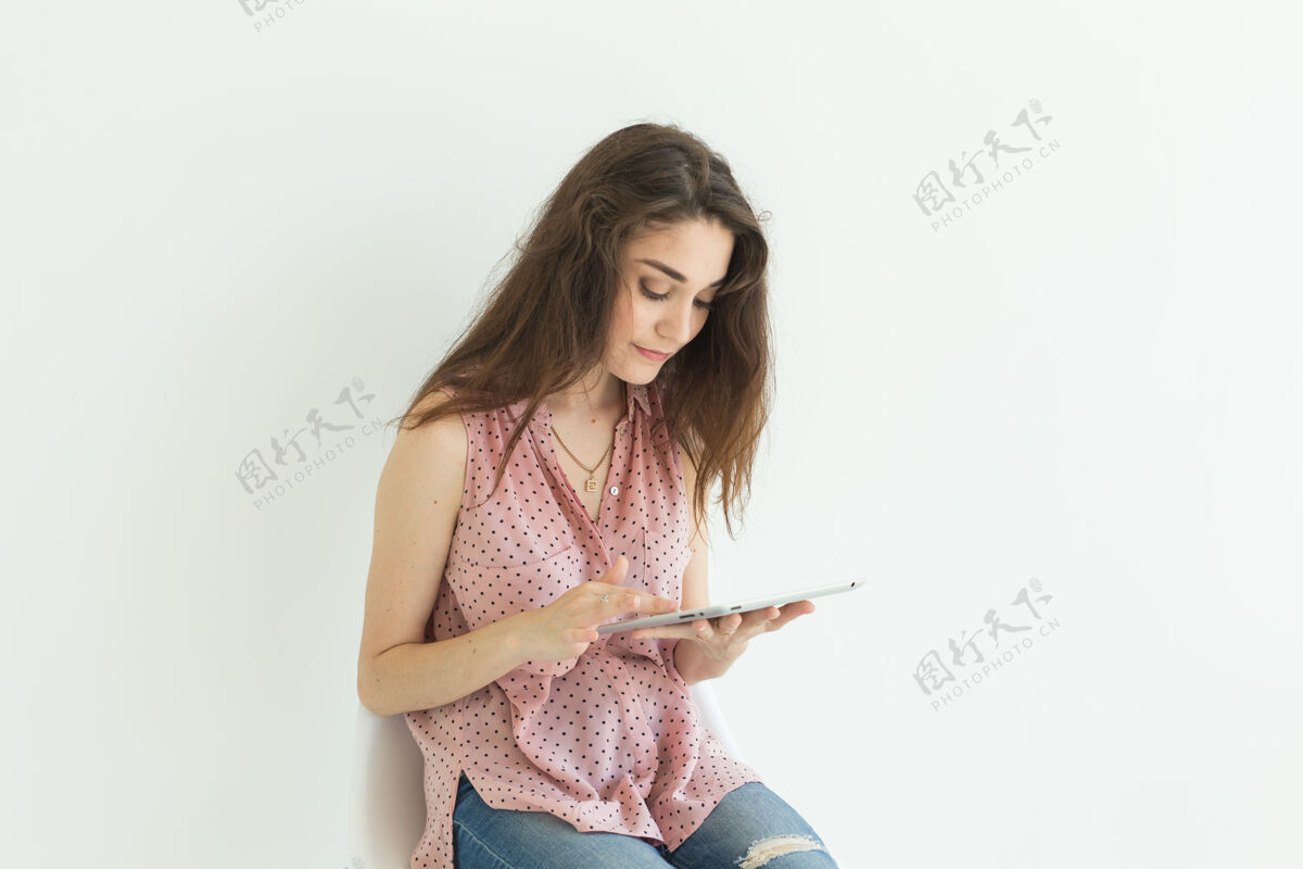 平板电脑坐在椅子上拿着白墙上的写字板工作的年轻女子网站快乐黑发