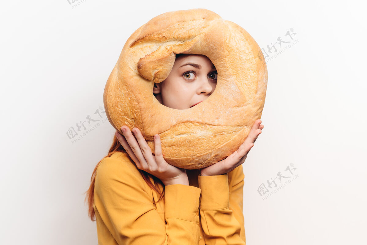 女人面粉制品圆面包和情绪化的女人在一个黄色衬衫上的光墙快乐咬欲望