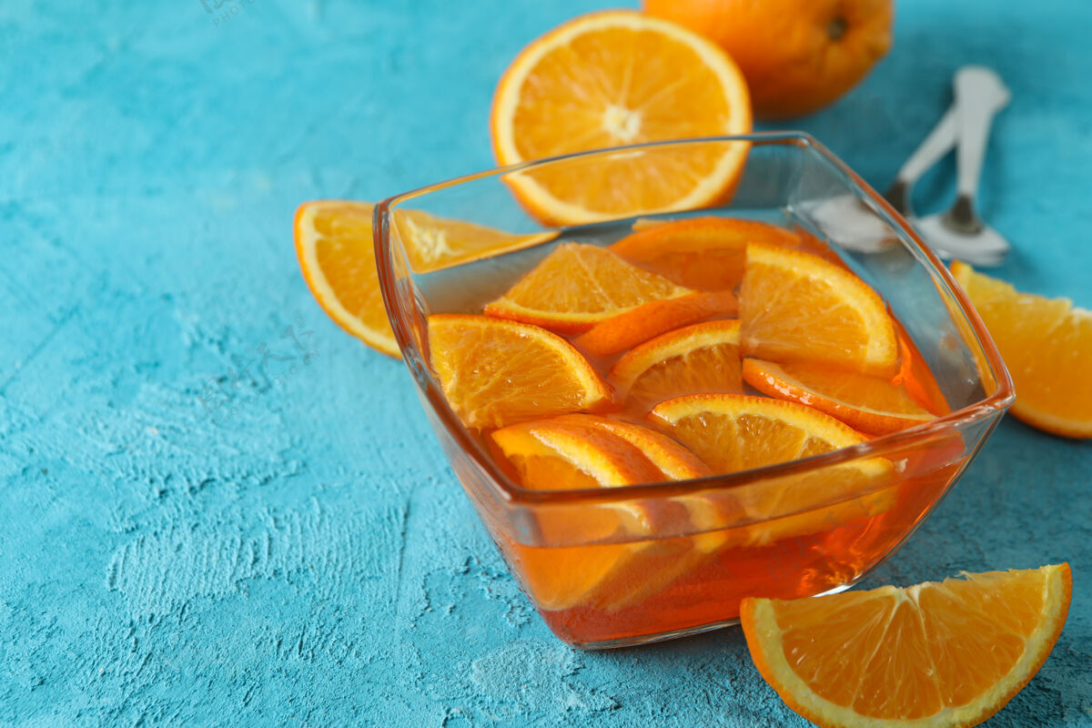 明胶一碗橙色果冻 蓝色纹理背景上有橙色切片凉美味甜点