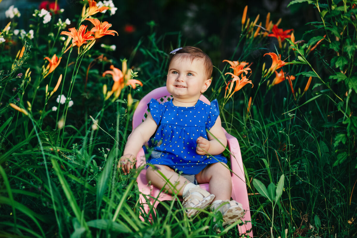 有趣可爱可爱的小宝宝穿着蓝色的裙子在满园的鲜花中微笑女性坐人