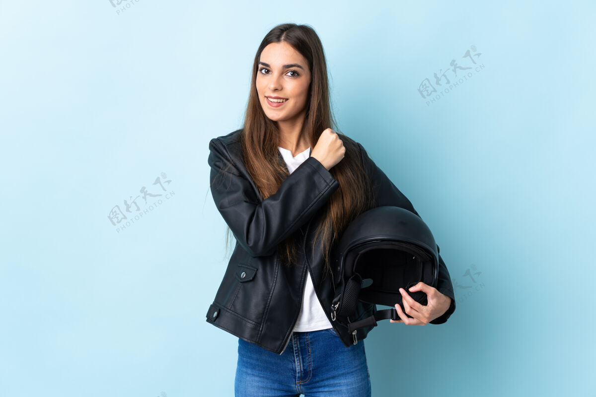 女孩年轻的高加索妇女手持摩托车头盔孤立在蓝色背景庆祝胜利女人胜利女性