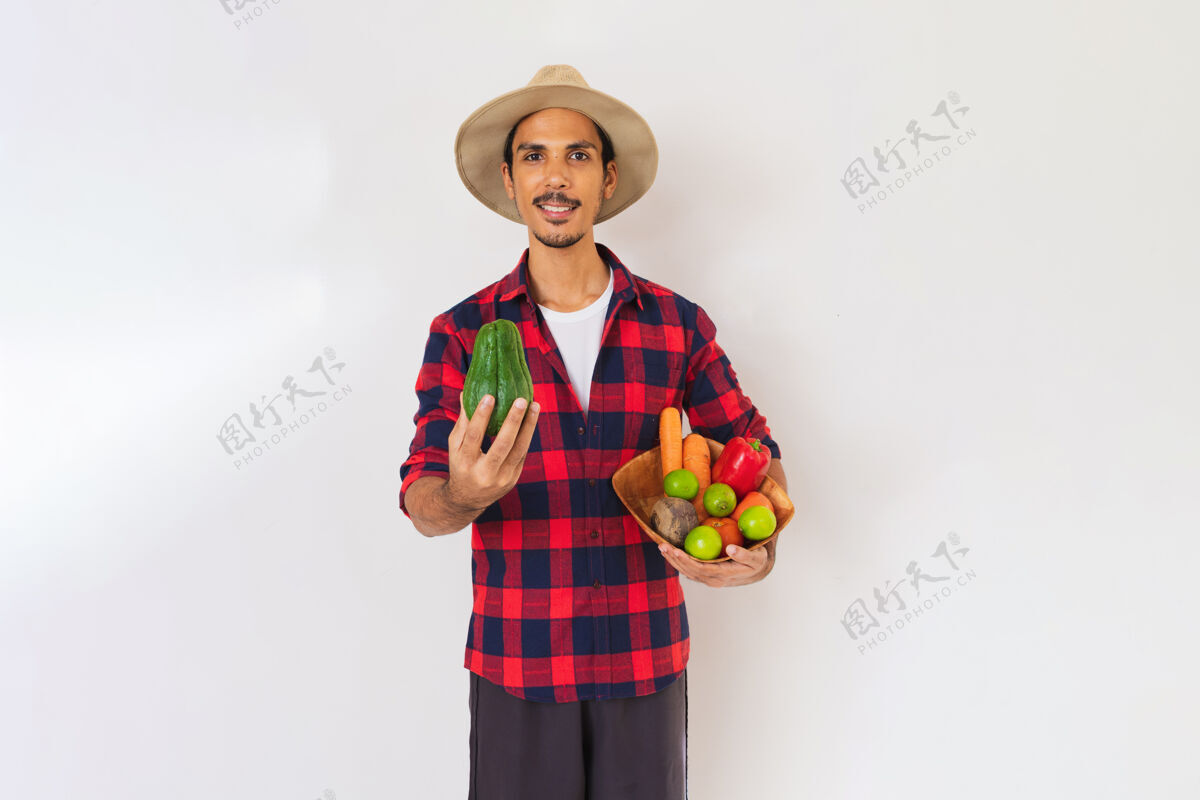 男人一个戴着帽子和手套的黑人农民手里拿着一篮子蔬菜（胡萝卜 柠檬 西红柿 佛手瓜和甜菜） 背景是白色的欢呼微笑食物