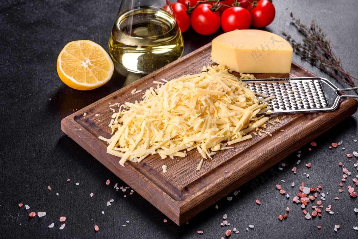 新鲜新鲜的硬奶酪磨碎在一个大的磨碎机在一个黑暗的混凝土背景木制砧板烹饪脂肪饮食