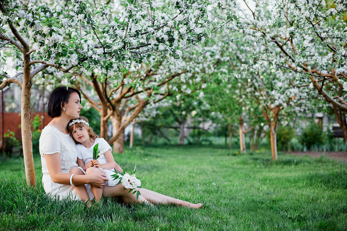 父母可爱的女儿和妈妈坐在春天的花园里拥抱爱草欢乐