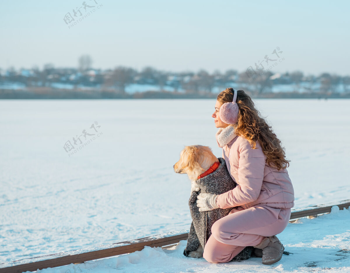 拉布拉多冬日冰河上的年轻女子和她的金毛狗坐在一起猎犬女人在户外和狗玩狗年轻休闲