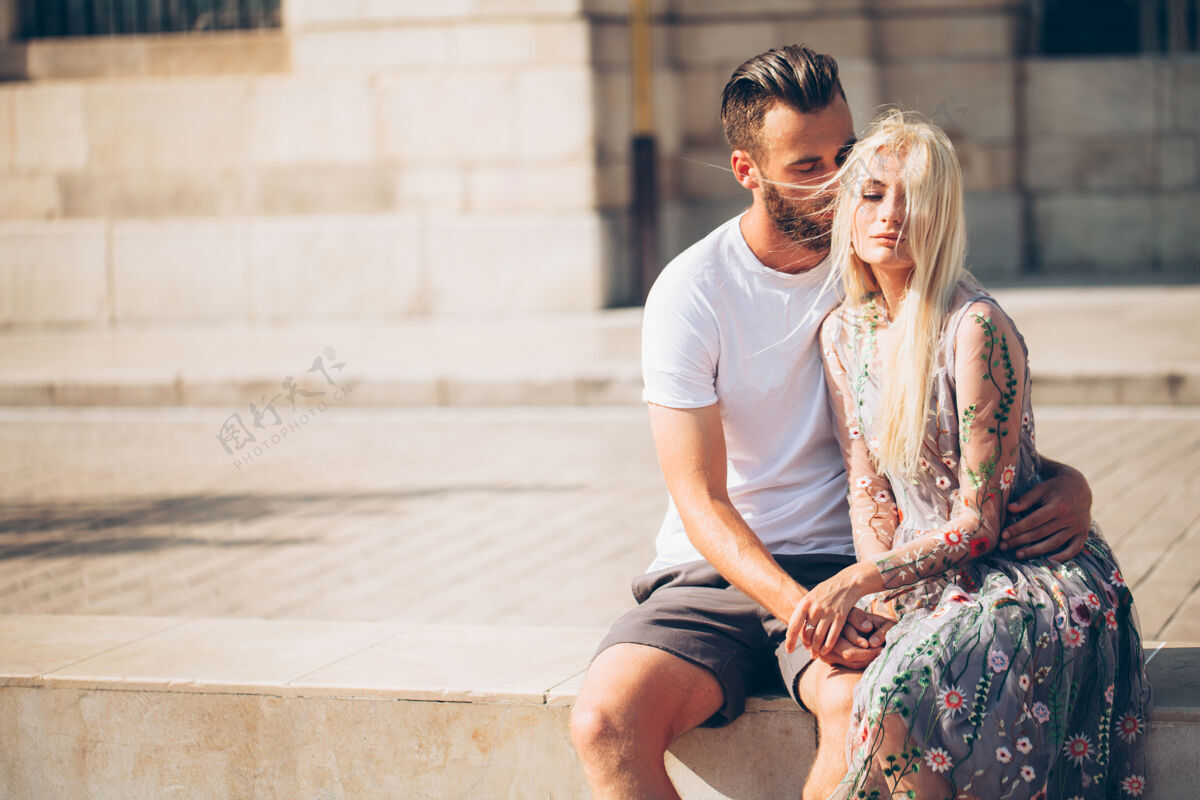 浪漫金发女孩和时髦帅哥胡子拥抱和亲吻在城市街道上美丽人城市