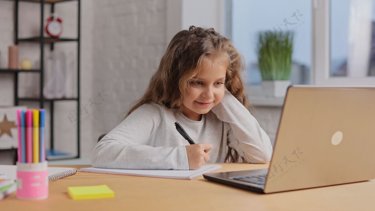 女孩可爱的小学生在家用笔记本电脑学习电脑女学生有在线课程讲座家庭作业课程