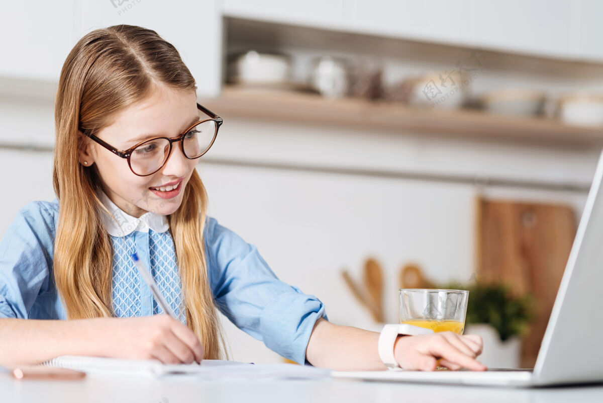 课寻找指南.明亮积极漂亮的女孩在做家庭作业和做笔记的时候用电脑世代房子厨房