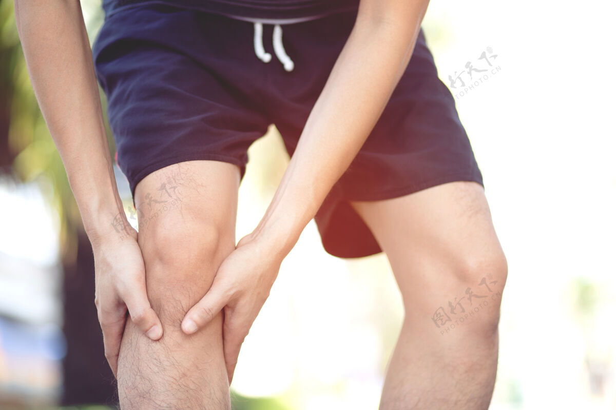 疼痛运动概念造成的伤害：亚洲人在公园的公路上跑步时 双手放在膝盖上健康腿慢性