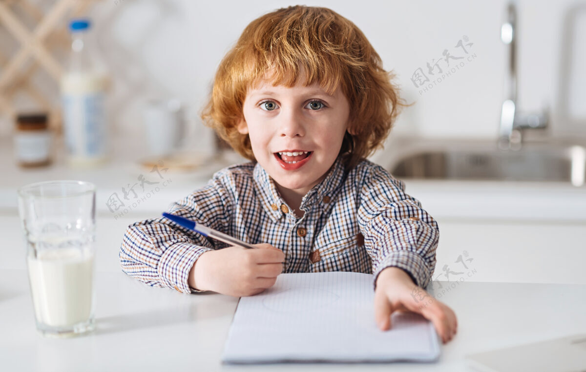 自我早晨小鸟可爱可爱聪明的孩子坐在亮白色的桌子旁写着什么 旁边的桌子上放着一杯牛奶有趣房子时间