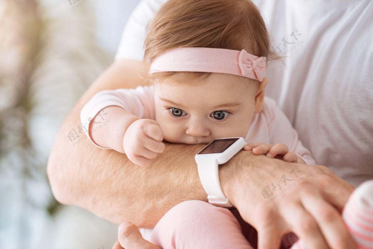 可爱充满注意 亲爱的可爱的女婴躺在爸爸的手里 一边看着别处 一边表达着兴趣和喜悦技术内部父母