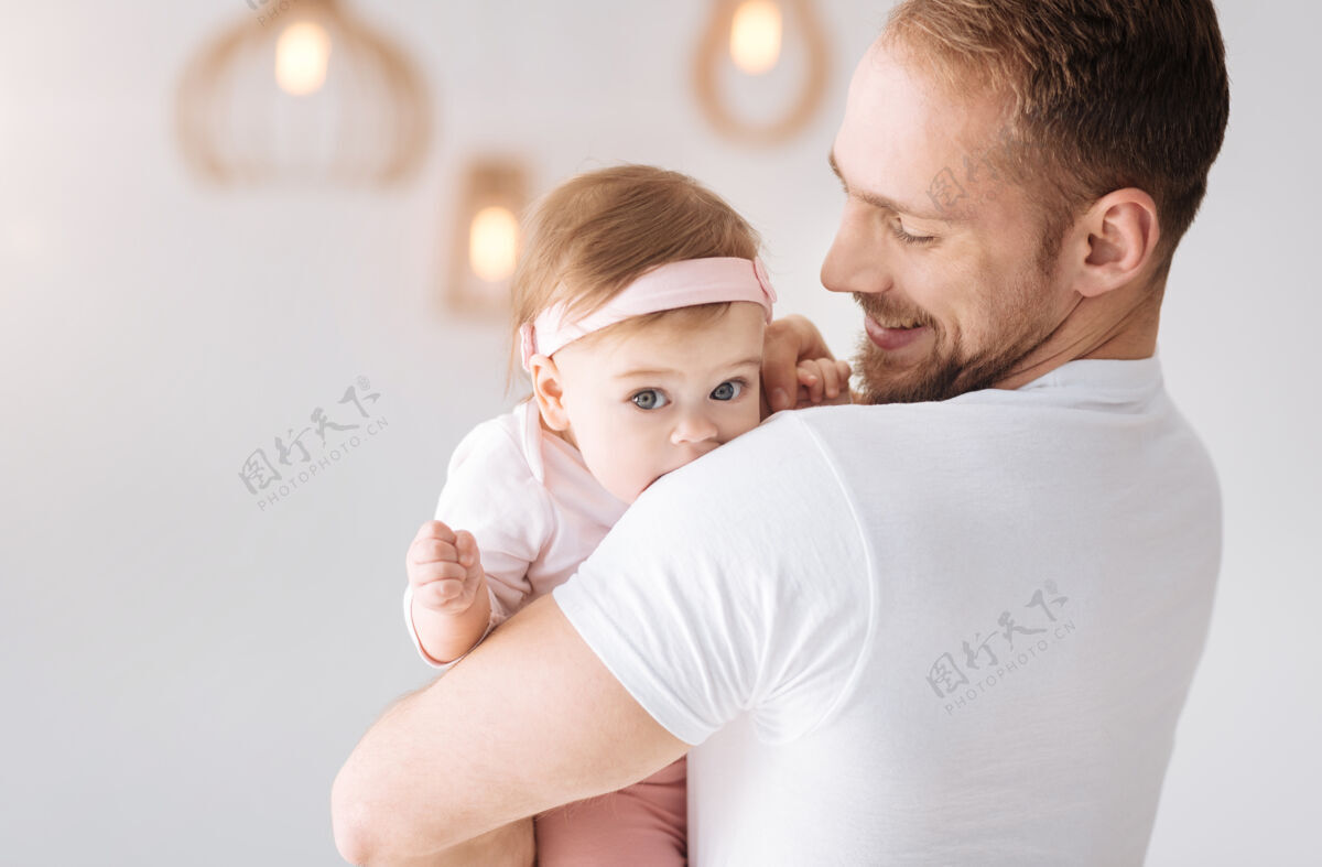 当代我可爱的孩子快乐高兴的胡须父亲站在家里 拥抱着蹒跚学步的女孩 同时表达温柔的情感白天新生儿女儿