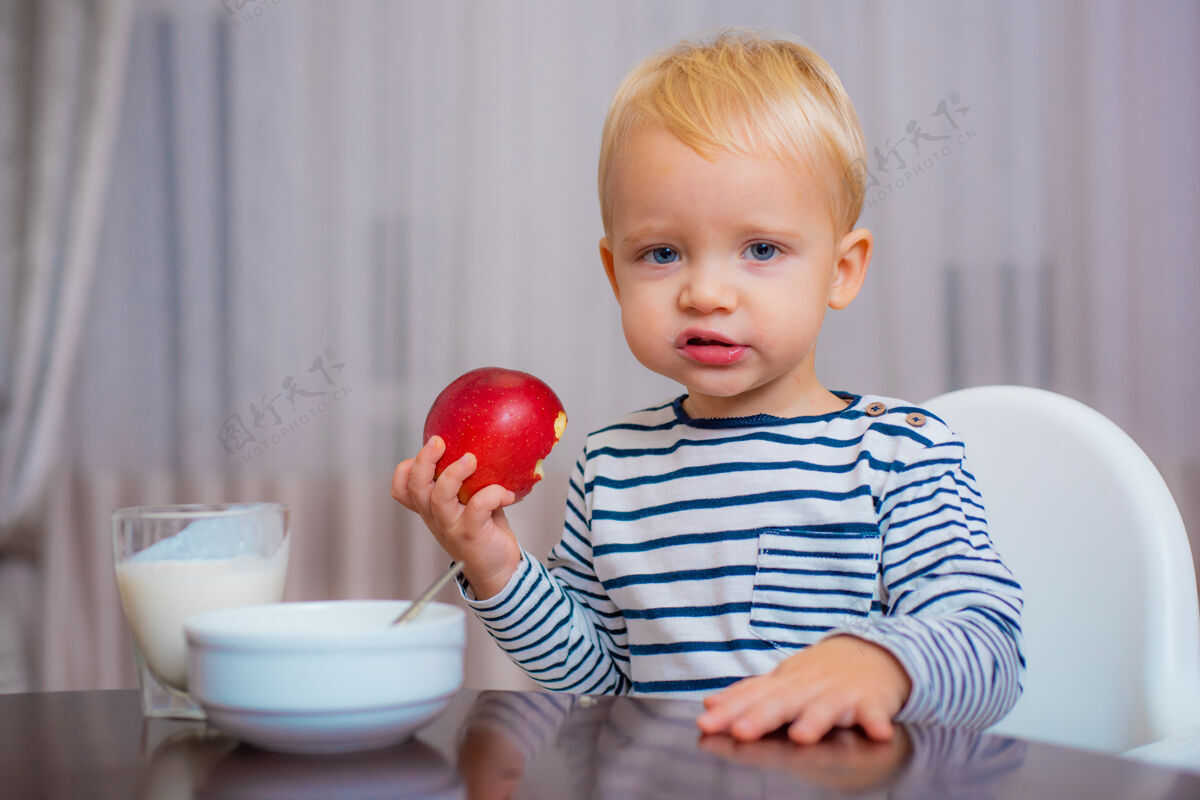 维生素可爱的蹒跚学步的孩子正在吃饭 手里拿着一个苹果 微笑着可爱年轻小