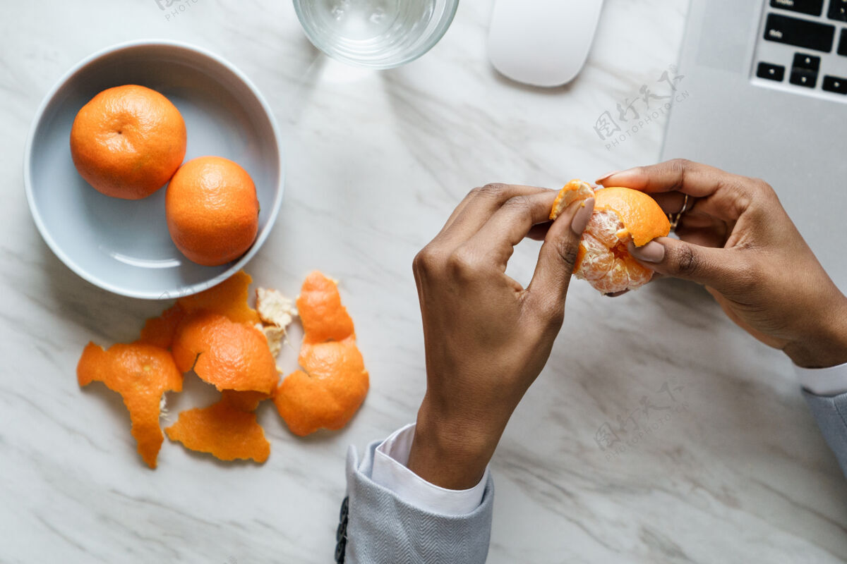 水果非洲裔女员工手剥熟甜橘子 穿西装 坐在办公桌前工作盘子食物果皮