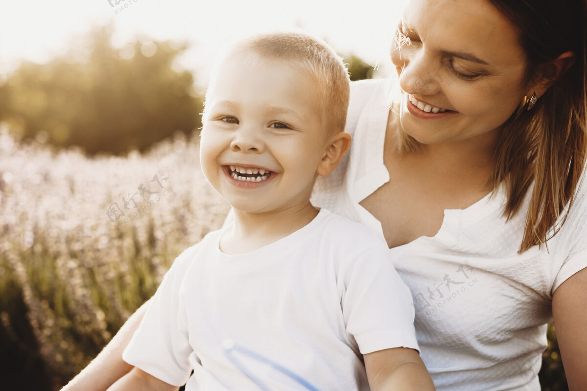 特写一位美丽的母亲在花丛中玩耍时看着她的小太阳的画像口腔科成人微笑