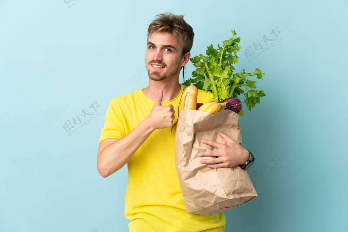 有机一个金发碧眼的人拿着一袋外卖食物 孤立地站在蓝色的一边竖起大拇指人帅哥农场