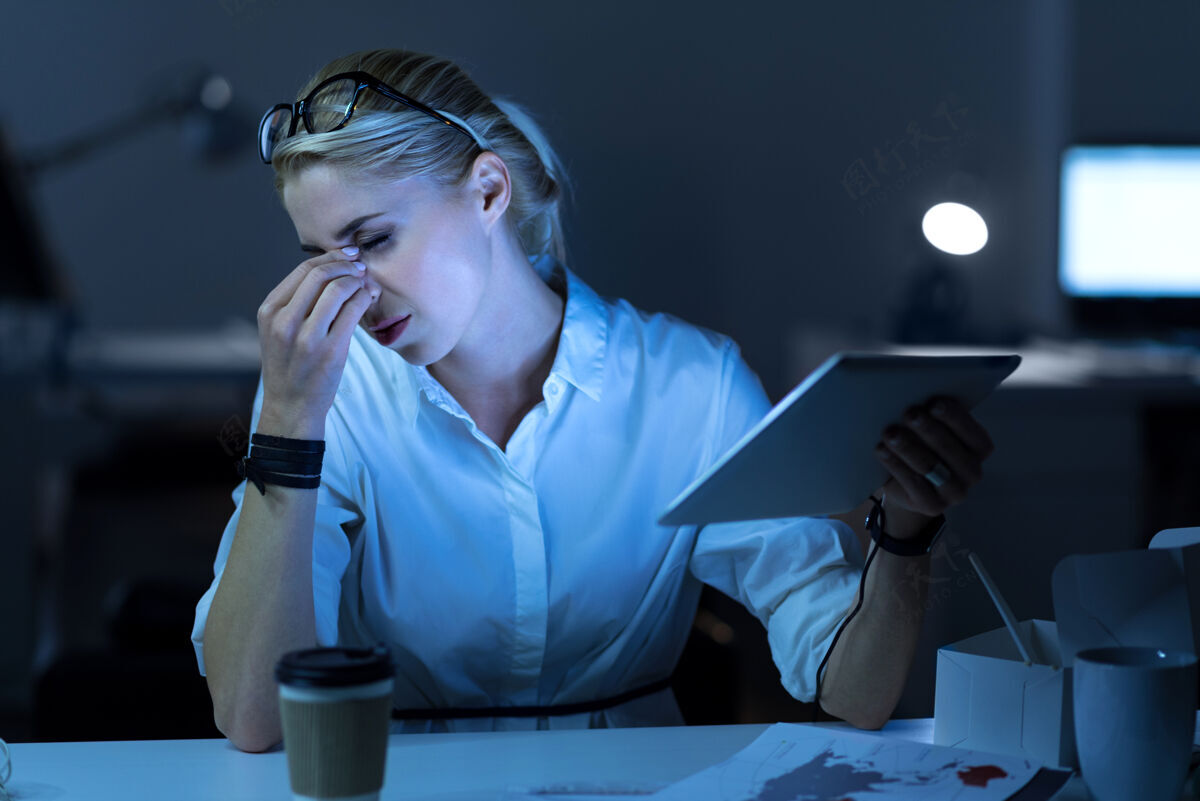 薪水长期工作卧倒的小时数疲惫的it女士坐在办公室里拿着平板电脑 一边做着项目 一边摸着头黑客千禧一代电子