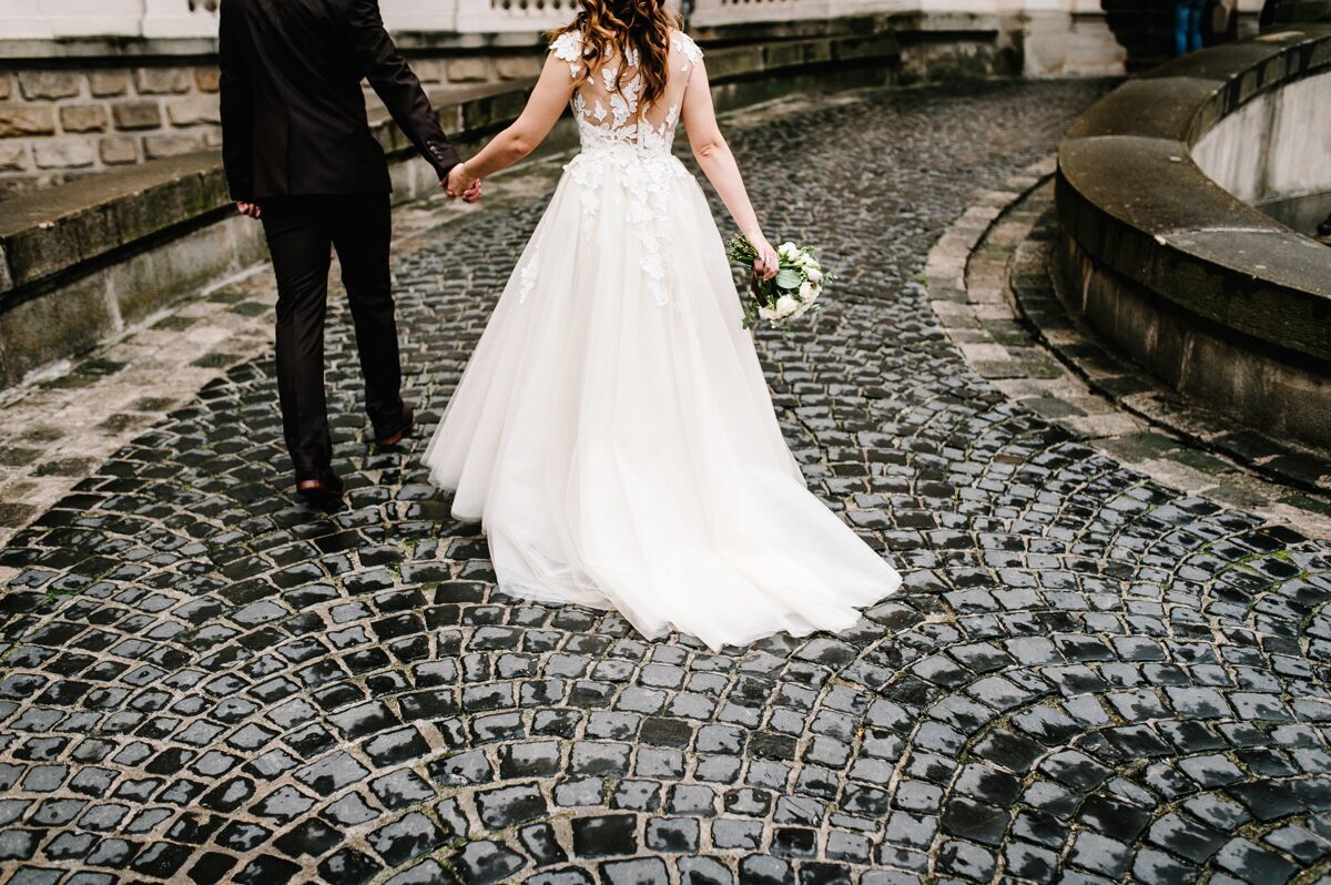 浪漫旧的新娘礼服和新郎西服的底部城市新婚夫妇带着一束婚礼花束 回到一条古老的石路上的宫殿新娘男性零件