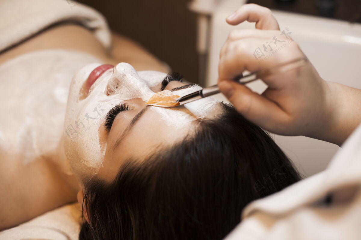健康美容美容师手敷白色护肤面膜在一个可爱的女性脸上在一个健康度假村女孩沙龙奢侈品