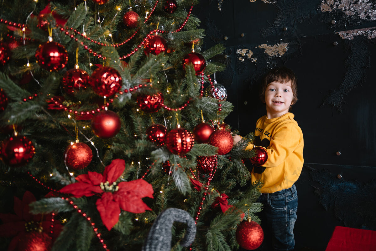 十二月一个快乐可爱的小男孩站在圣诞树旁 手里拿着一份礼物盒子孩子圣诞节心情.假期.圣诞节新年快乐微笑拇指圣诞老人