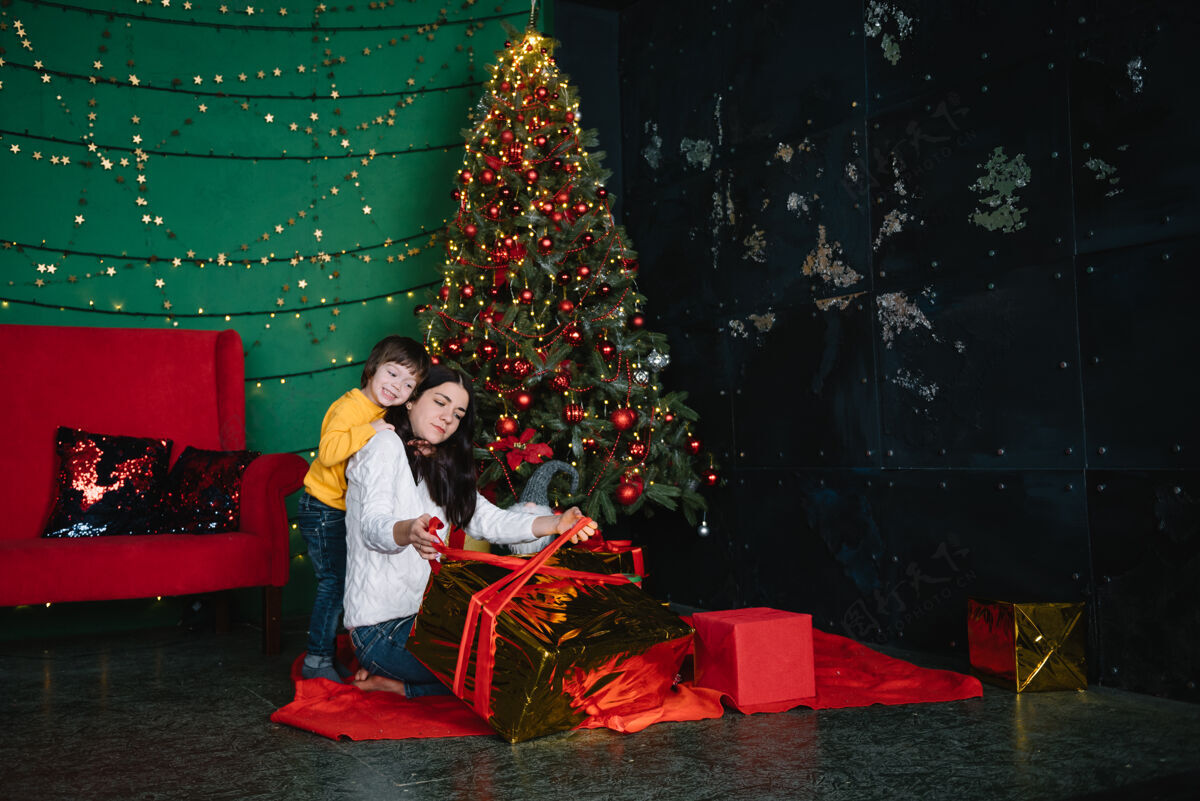 房子年轻美丽的母亲带着可爱的儿子在圣诞树旁礼物快乐圣诞节妈妈阁楼男孩