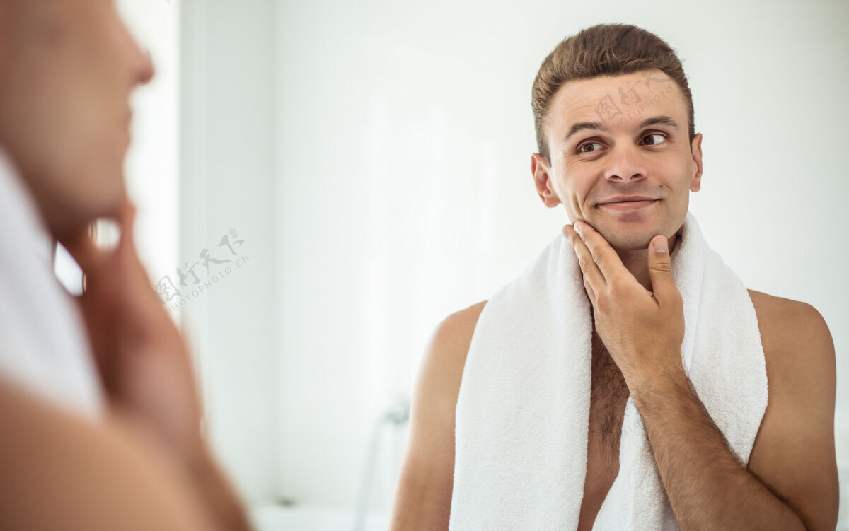 留茬英俊的年轻人在街上刮胡子浴室.肖像一个时髦的裸体胡须男人在家里的镜子里检查他的脸男人镜子反射