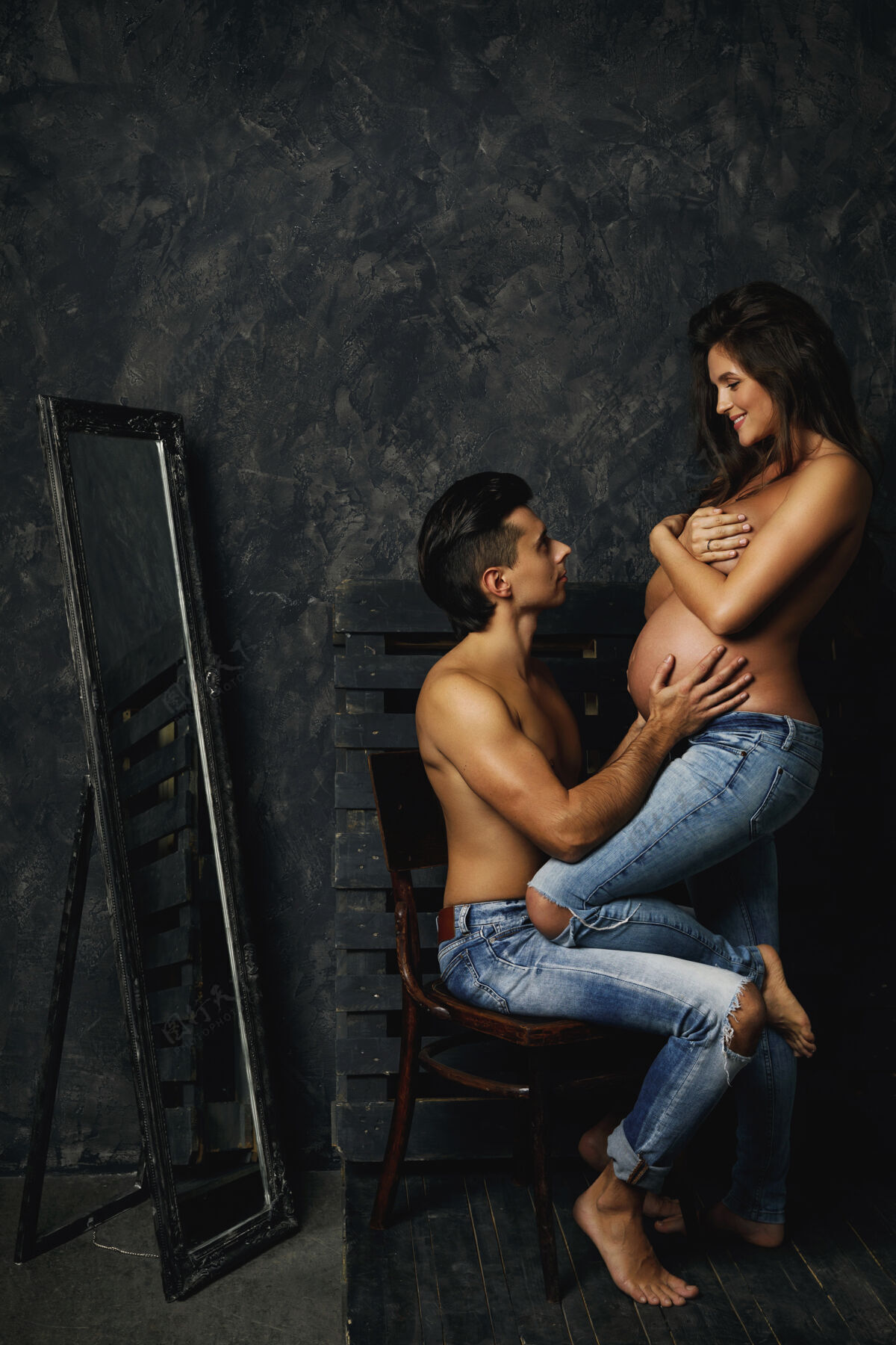 牛仔裤性感的年轻夫妇在等着宝贝男人还有他怀孕的妻子在室内摆姿势婴儿裸体护理