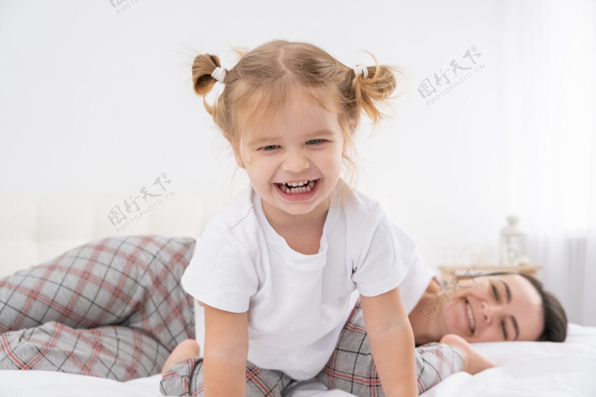 乐趣成年妈妈在家里和活泼的小女儿在床上玩耍 和孩子们一起玩 一起活动一起家庭玩