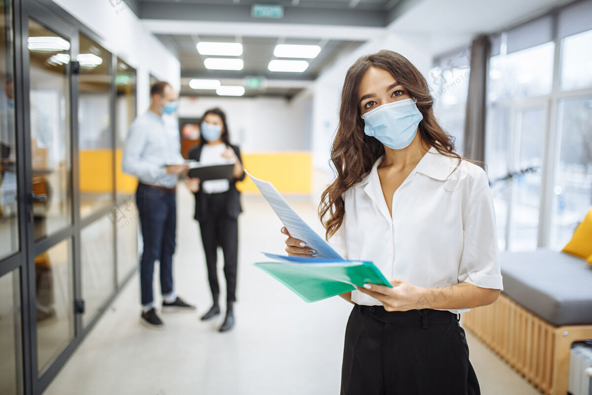 企业家一个年轻的女商人戴着医用口罩 在办公室走廊里查看报纸和商业趋势和前景的画像社会距离团队平板电脑
