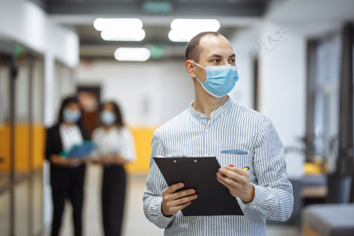 预防优雅的商人戴着医用口罩站在办公室走廊里 手里拿着一块药片男性工人流行病