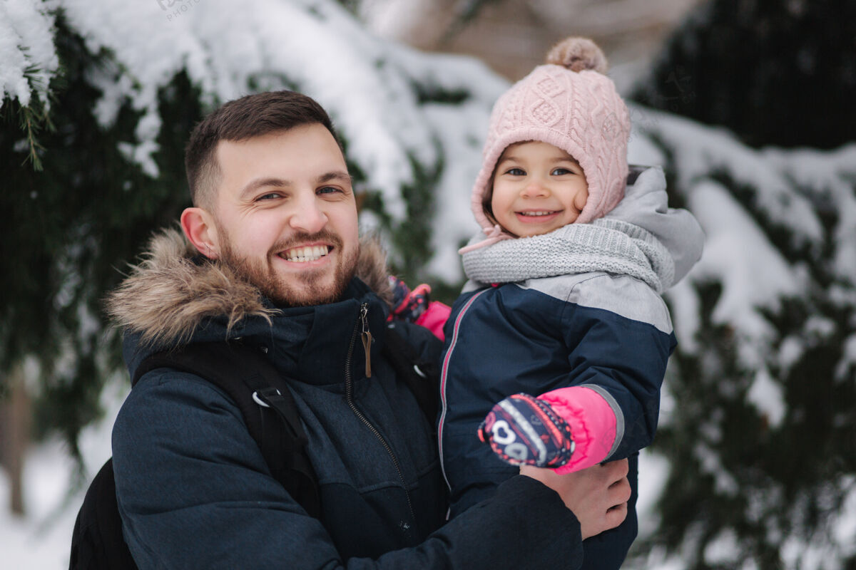 休闲可爱的小女儿和她可爱的爸爸站在雪树旁雪橇雪散步