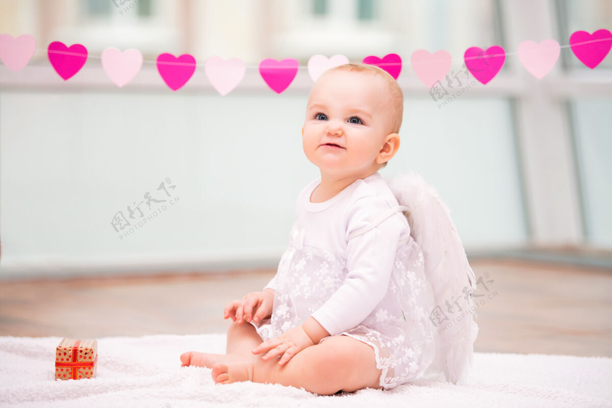 微笑一个快乐淘气的婴儿的肖像 长着白色天使的翅膀心天天使