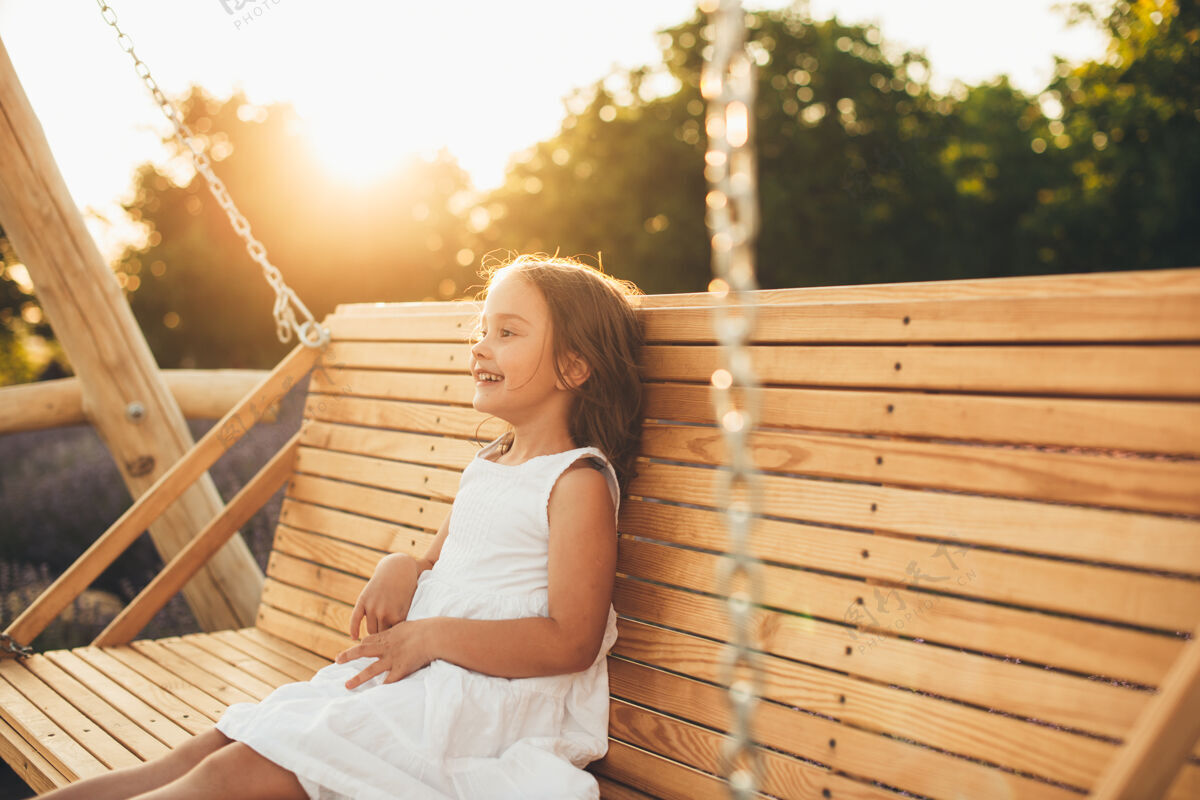 光可爱的小女孩一边笑一边在户外的木制秋千上享受日落的乐趣童年肖像休闲
