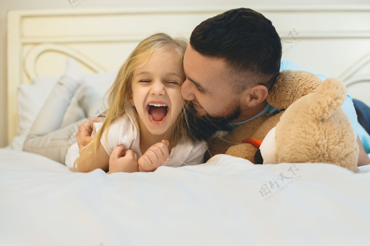 父母可爱的金发小女孩早上在家里的床上和爸爸玩的时候笑了教育可爱玩耍