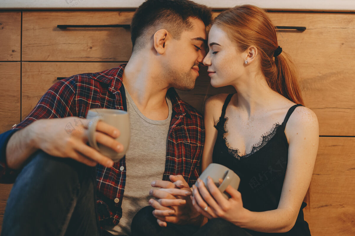 公寓迷人的年轻白种人夫妇坐在厨房的地板上 面对面亲密地亲吻 然后在家喝咖啡室内雀斑女人