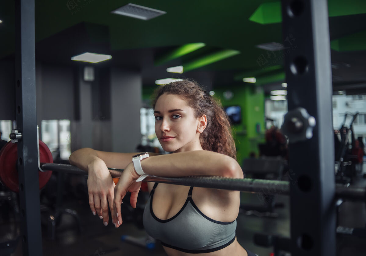 肌肉一个穿着运动服的疲惫的女人在体育馆里靠着杠铃筋疲力尽减肥举重