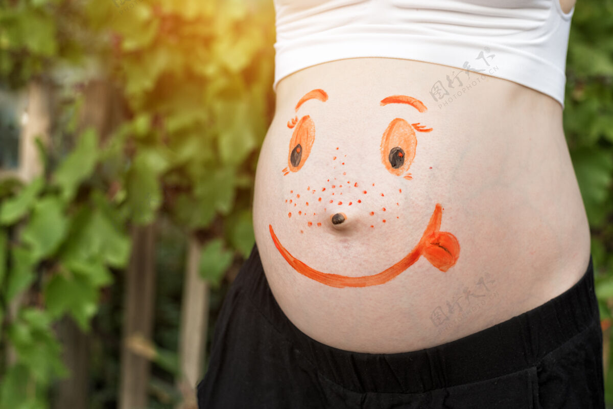 怀孕孕妇的肚子上画着微笑脸绿色背景等待家庭护理