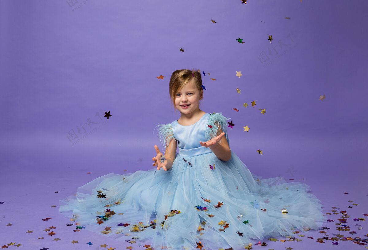 欢呼一个小女孩坐在一个美丽的公主礼服和捕捉五彩纸屑紫色可爱时尚嘉年华