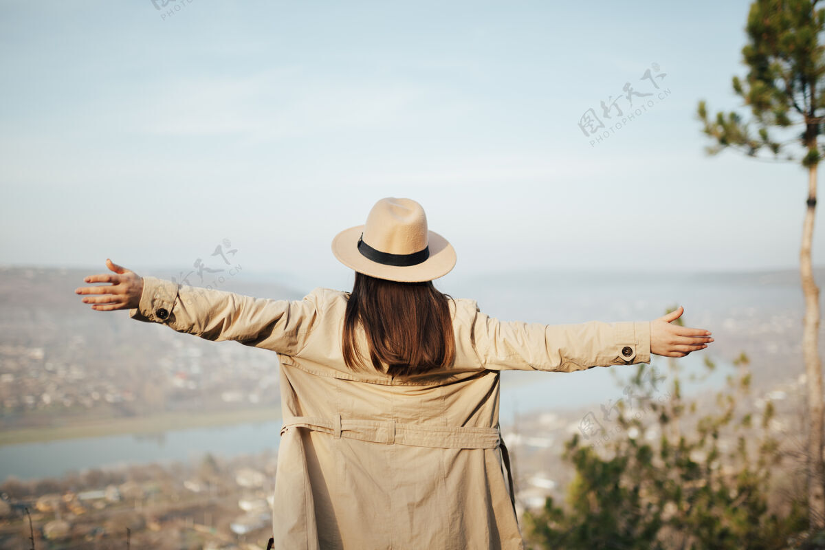 徒步旅行年轻女子站在山顶上 手举着手 从上面看城市姿势自由顶