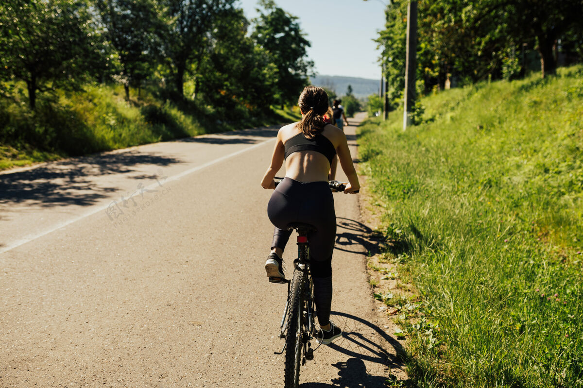 自行车在阳光明媚的夏日 穿着时尚运动服的美丽年轻女子骑着自行车在柏油乡村公路上驰骋运动自由女人