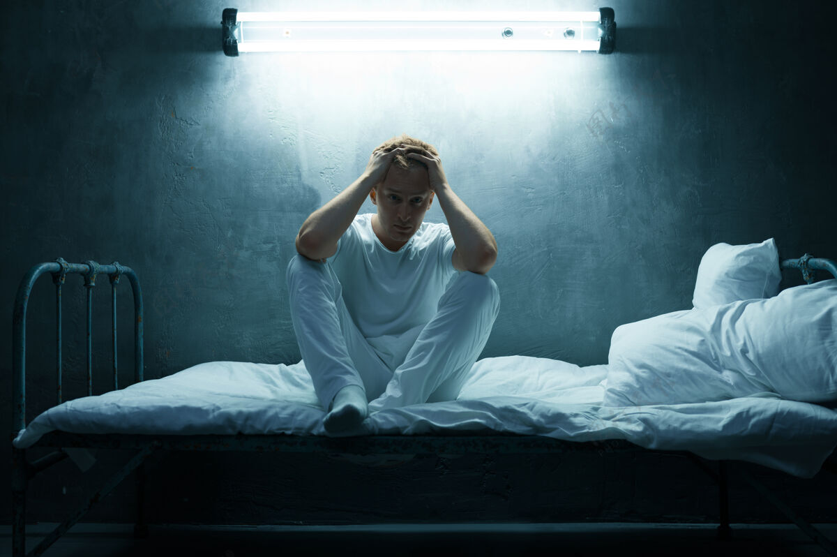 不快乐坐在床上的神经病男人 黑黑的房间迷幻药每晚都有问题的人 抑郁和压力 悲伤 精神病院光幽灵问题