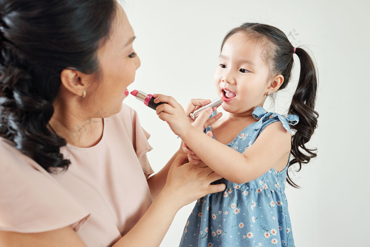 父母快乐的亚洲母女在早晨准备的时候互相涂唇膏孩子香膏微笑
