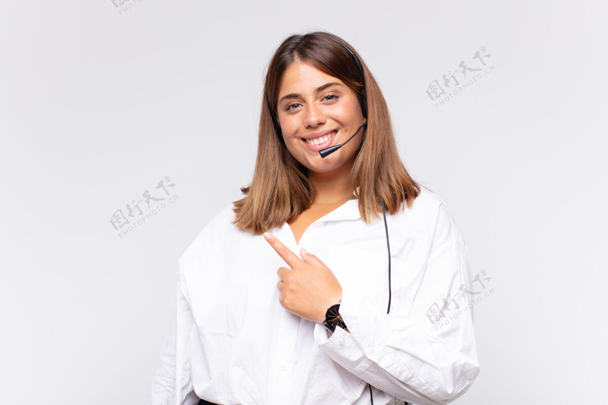 成人年轻的女电话销售员愉快地微笑着 感到高兴 并指向侧面和向上 显示复制空间的对象身体助理年轻人