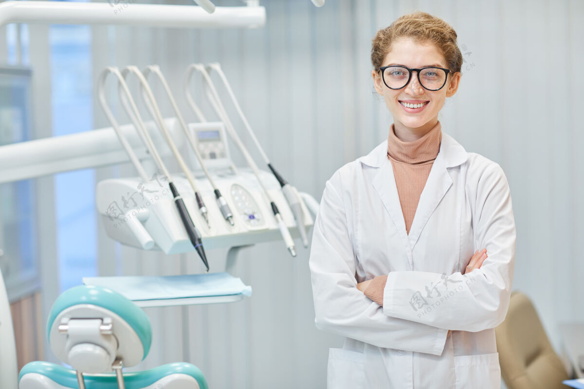实验室身穿白大褂的年轻牙医站在牙科诊所前交叉双臂微笑的画像牙医办公室设备实验室外套
