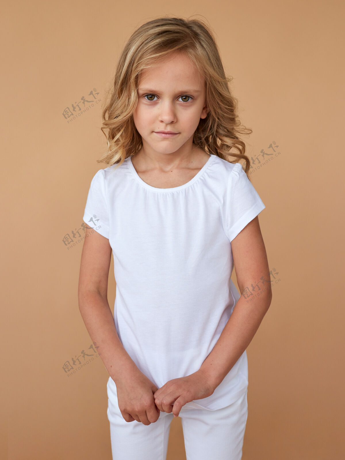 小前面是一个穿着白色衣服 头发卷曲 胆小可爱的小女孩的肖像服装.时尚照片.垂直查看童年孩子年轻